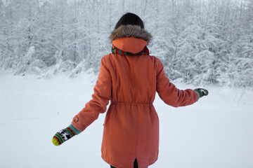Woman wearing orange hooded coat and yellow mittens with deers walks in a winter forest. People from behind. Snowy forest background. Winter traveling lovers concept. © Intergalactic Rada
