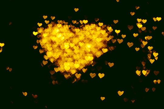 Unfocused image of Love heart sign, consist of small shining heart shapes on black background. Greeting card for Valentine's day. Glamorous luxury golden heart with copy space.