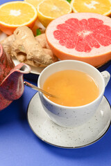 Tea cup and tea pot with cut citrus fruit over blue background. Tea time, healthy lemon and grapefruit drink concept.