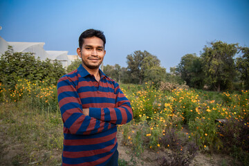 Portrait of Young smiling indian farmer standing at hi farm, copy space, man with cross arm. agriculture.