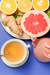 Tea cup and tea pot with cut citrus fruit over blue background. Tea time, healthy lemon and grapefruit drink concept.