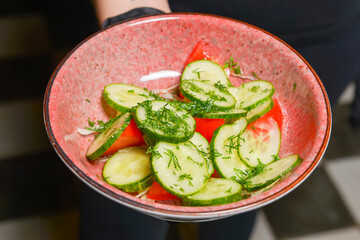 Vegetable cucumber and tomato salad with oil served by waiter in restaurant or diner.