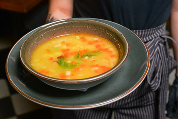 Fresh vegetable soup in bowl served by waiter in restaurant or diner. Eating out concept, meal for dinner.