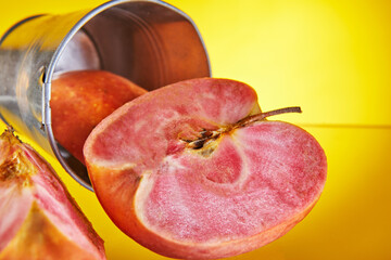 An apple with red pulp inside with a carved wedge on the background of a bucket. Yellow background isolated. Exotic fruits, healthy food