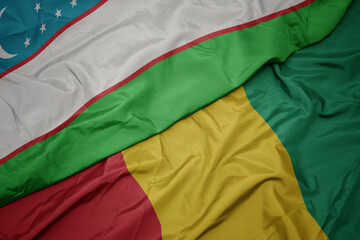 waving colorful flag of guinea and national flag of uzbekistan.