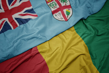 waving colorful flag of guinea and national flag of Fiji .