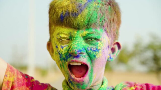 Close up head shot of Boy kid shouting during holi festival celebration with color applied to face - concept holi festive celebration, joy and enjoyment.