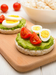 Rice cakes with avocado mash and eggs with tomato on cutting board vertical shot