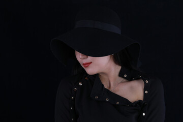 Fototapeta premium close-up studio portrait of a beautiful girl in a black hat on a black background
