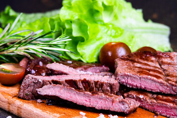 black angus steak with tomatoes, rosemary and lettuce on a board
