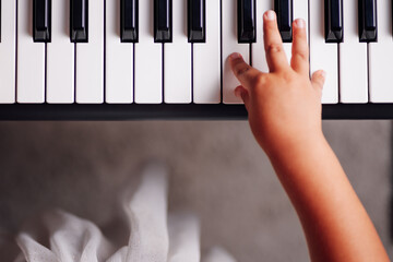 top view of a girl's hand pressing the keys of an electronic synthesizer in the living room with...