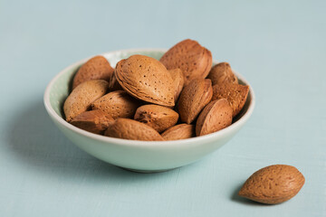 Pile of Almond nuts in a bowl on a light blue background. Fresh nuts in their shells.