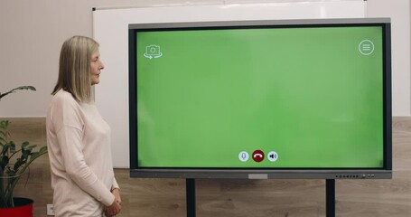 Mature woman using interactive screen with template green screen for communicating. Female professor talking and looking at digatal board in classroom. Concept of online learning.