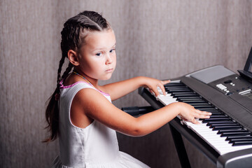 a pensive, dreamy girl in a white summer dress and two pigtails trains chords on an electronic...