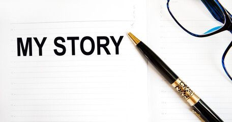 In the diary text MY STORY, next to the pen, glasses.