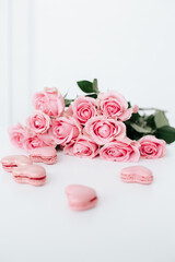 Pink roses on a white surface with pink heart shaped macaroons for anniversary
