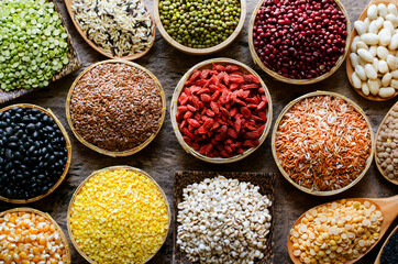 Collection of dry organic colorful cereal and grain seeds in wooden bowl in dark tone, for healthy food ingredient concept