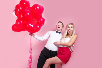 Valentines day. Happy young couple with heart shaped balloons on pink background.