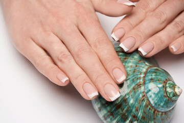 Beautiful Female well-groomed Hands with French manicure holding sea shell over light background