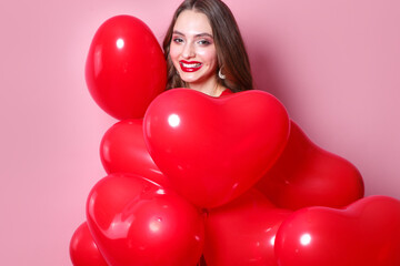 Woman on Valentines Day. Beautiful elegant young woman with heart shape red air balloons on pink background.