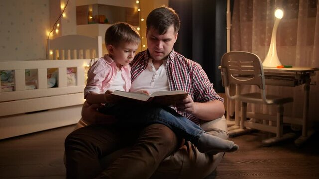 Smiling little boy listening to bedtime story his father is reading to him at night. Concept of child education and family having time together at night