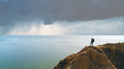 The hiker standing on the mountain against rainy clouds above the sea