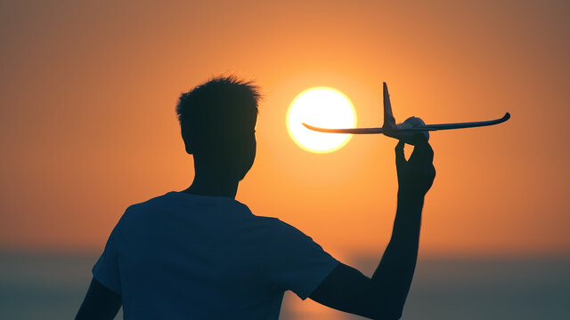 The man launches a toy plane on the sunset bakcground