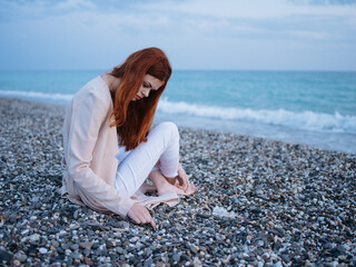 A traveler with red hair sits on the beach and looks at the ocean white foam transparent water