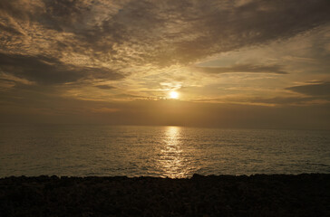 Obraz premium Sun rising above sea, clouds lit by yellow light
