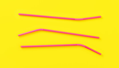 Three pink plastic drinking straws on yellow board, view from above