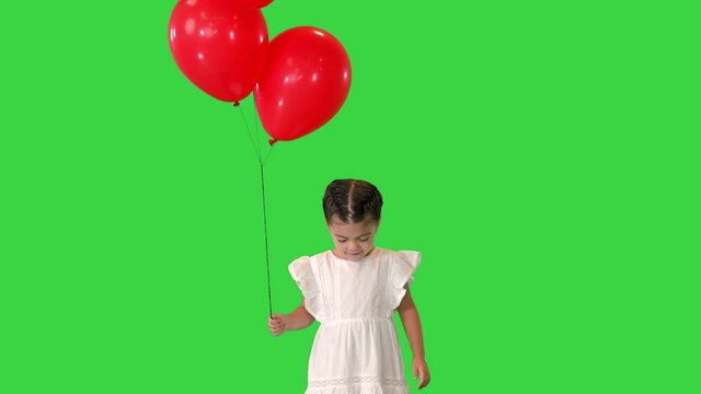 Adorable little girl holds tightly to a large bunch of helium balloons walking on a Green Screen, Chroma Key.