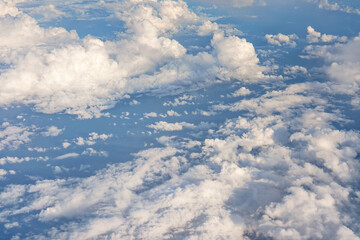 Fluffy sky clouds lit by afternoon sun, as seen from commercial airplane flying over