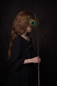 Classic dark renaissance portrait en profile of a redheaded girl with a peacock feather in front of her eye
