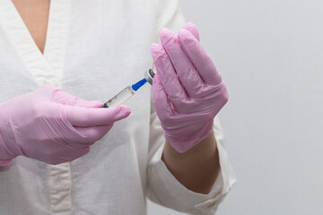 Close-up of the doctor's hands with a bottle and a vaccine, the vaccine is typed into a syringe. Medical concept vaccination subcutaneous injection treatment, prevention. On a white background.