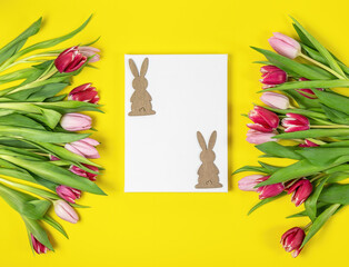 Easter frame of pink and red tulips and wooden bunny on yellow background. Top view with copy space. Happy Easter holiday. Greeting card.