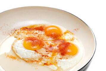 Fried eggs with ground paprika on frying pan isolated on white background