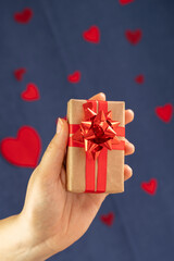Composition for Valentine's Day February 14th. Person holding out a gift with red ribbon, heart shape. close-up, be my valentine, valentines day gift express love.2021 concept. selective focus on box.