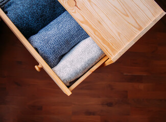 Open wooden dresser drawer with warm knitted woolen clothes. Home vertical storage. Wardrobe...