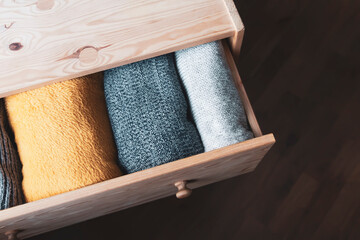 Open wooden dresser drawer with warm knitted woolen clothes. Home vertical storage. Wardrobe...