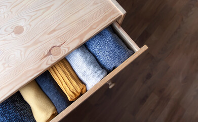 Open wooden dresser drawer with warm knitted woolen clothes. Home vertical storage. Wardrobe...