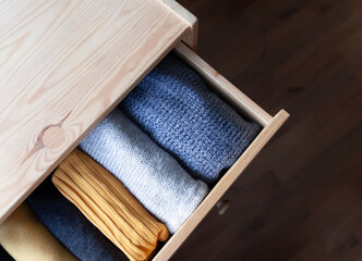 Open wooden dresser drawer with warm knitted woolen clothes. Home vertical storage. Wardrobe...