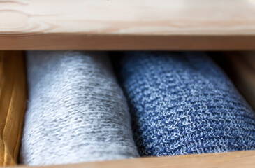 Fototapeta na wymiar Open wooden dresser drawer with warm knitted woolen clothes. Home vertical storage. Wardrobe organizing.