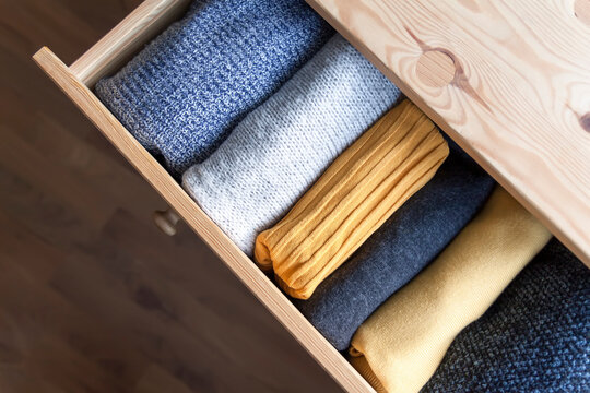 Open wooden dresser drawer with warm knitted woolen clothes. Home vertical storage. Wardrobe organizing.