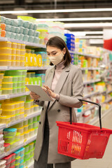 Young elegant female consumer choosing plastic container while using tablet