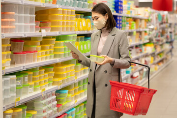 Young Asian female consumer with red shopping basket using tablet in supermarket