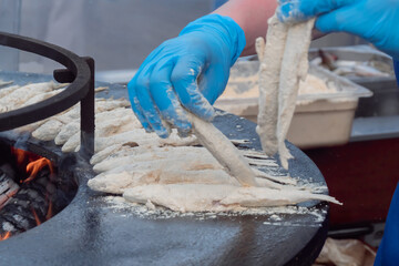 Chef hand cooking european smelt fish in flour on black brazier at summer outdoor food market:...