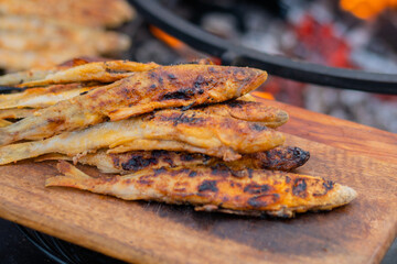 Crispy breaded european smelt fish on wooden cutting board at summer outdoor food market: close up. Seafood, barbecue, gastronomy, cookery, street food concept