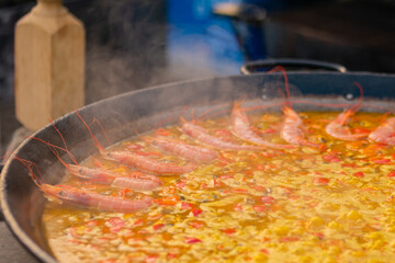 Process of cooking paella with shrimp, mussel, rice, spice, saffron in huge paella pan at summer outdoor food market - close up. Spanish cuisine, seafood, gastronomy, street food concept