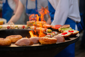 Preparing shrimp, prawn skewers and burgers with red caviar, avocado on brazier with hot flame at summer local food market - close up. Outdoor cooking, seafood, gastronomy, street food concept