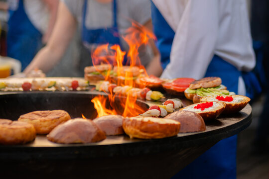 Preparing shrimp, prawn skewers and burgers with red caviar, avocado on brazier with hot flame at summer local food market - close up. Outdoor cooking, seafood, gastronomy, street food concept